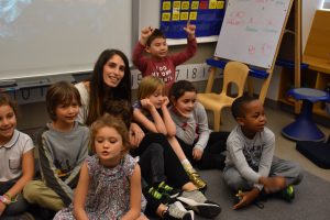 A group of students sit on the floor to pose with their teacher. 