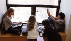 Four students sit together by a window doing schoolwork.