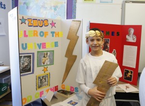 A student stands next to his presentation about Zeus, dressed in Roman costume.