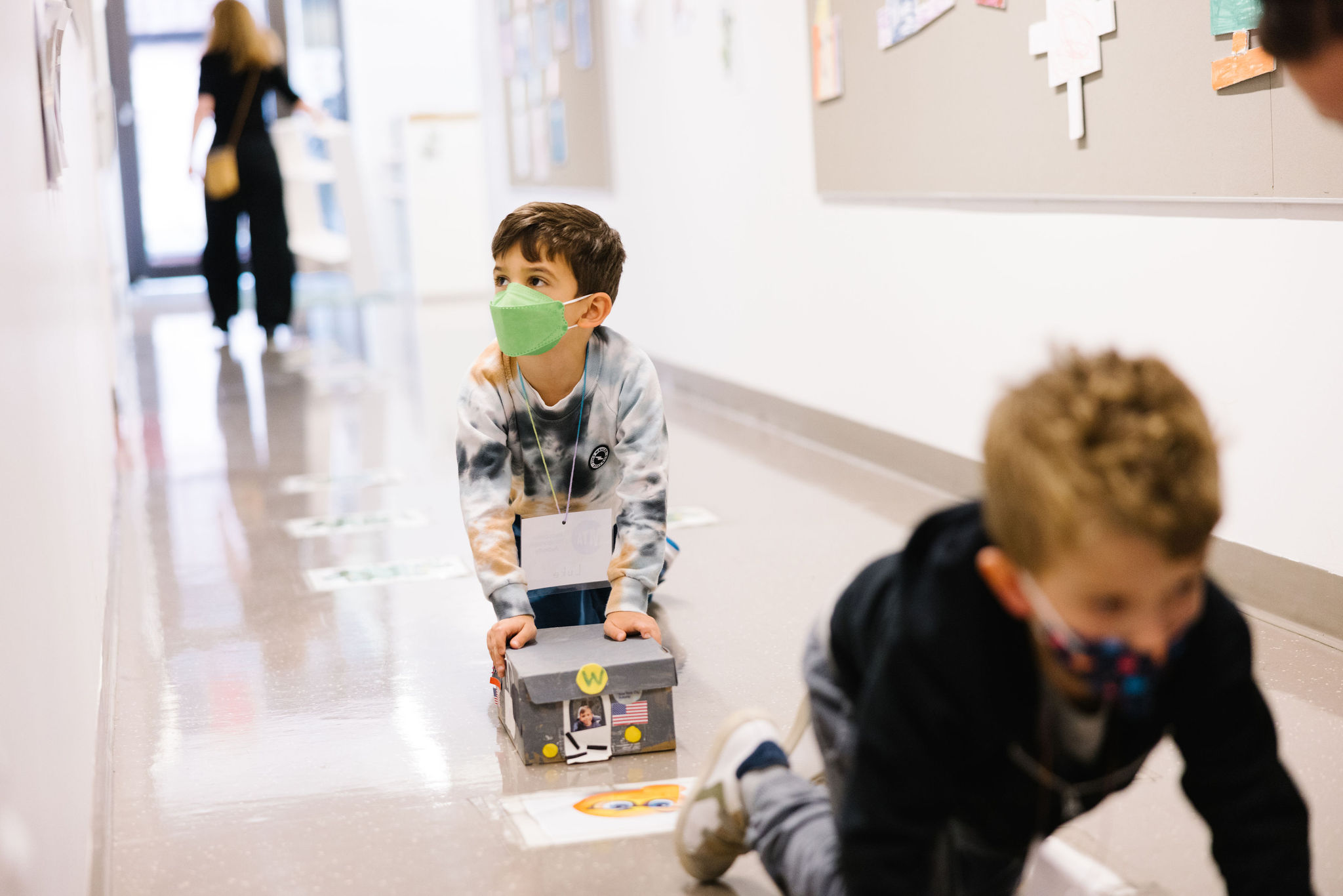 Students on the floor push their handmade subway cars through the hallway.