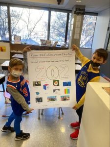 Two students hold a poster with the title "Room 202's Classroom Charter". 