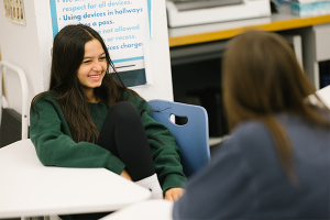 Student sitting at desk smiles at other student who is out of focus