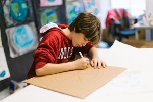 Student draws a wheel onto a sheet of brown paper