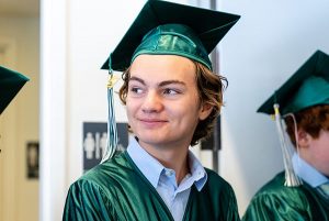 Student in green graduation cap and gown smiles at something out of frame