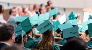 Rows of students photographed from the back wearing green graduation caps