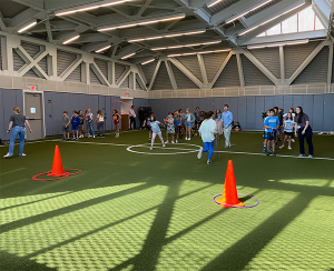 Students in field house tossing hula hoops onto orange cones