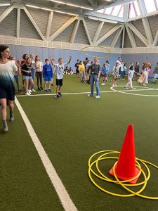 Student tossing yellow hula hoop onto orange cone