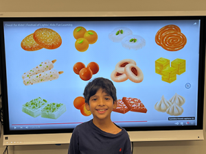 Student stands in front of paused video displaying sweets for Diwali