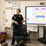 Police officer stands in front of Smartboard with a slide that reads "Welcome Police"