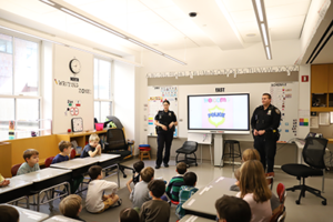 Two police officers stand at the front of the room before a group of Pink Cluster students