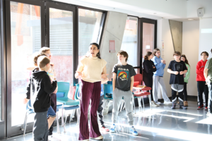 A Teaching Artist stands inbetween two students in front of windows in the North Cafeteria