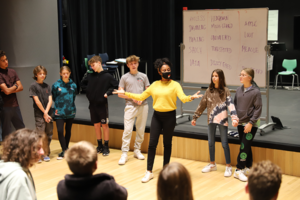 Teaching Artist instructor stands in an oval with students in front of the stage in Gaynor's Performing Arts Center