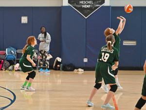 Three members of the volleyball team on the court; two are bending their knees to get ready while one sets the ball