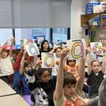 students hold up signs with vowel sounds in a multisensory phonics lesson