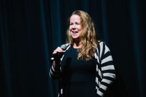 Assistant Head of School Jill Thompson holds a microphone in front of stage curtains in Gaynor's Performing Arts Center.