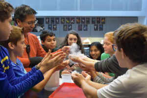 Andrew Prasarn holding a block of liquid nitrogen up to students gathered around a table.