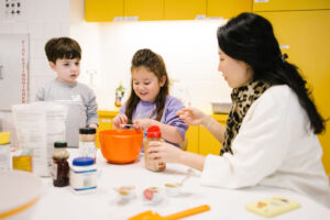 EC students sitting at a table surrounded by baking ingredients. Student in center is holding a teaspoon full of cinnamon over a bowl.