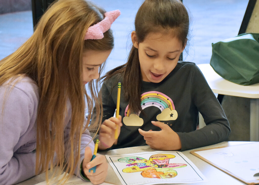 Two students bent over a table, reviewing another student's artwork