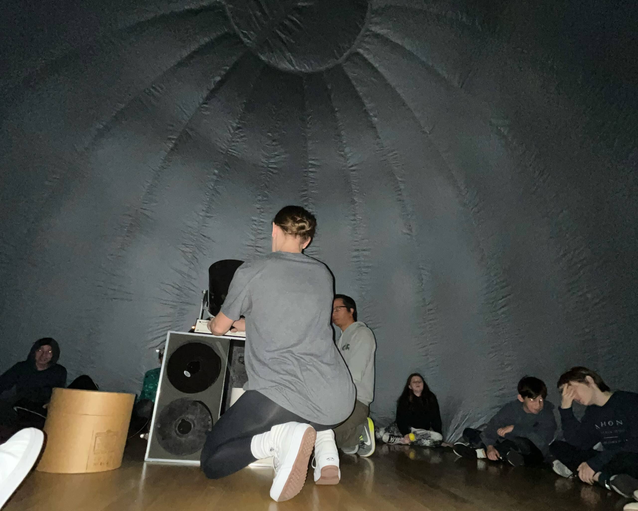 STEM Specialist Molli Grady helps prepare the StarLab projector. Students sit on the outer edge of the StarLab's interior.