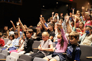 Students in an assembly raising their hands