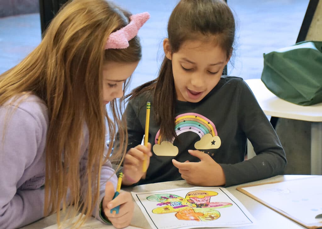 Two students bent over a table, reviewing another student's artwork
